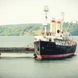 Stary statek "Angara" cumuje przy nabrzeżu. W tle zielone wzgórza i spokojna woda. Port nad Angarą.