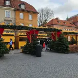Jarmark świąteczny Warszawa: drewniane budki ozdobione choinkami i lampkami, ludzie spacerują wśród świątecznych dekoracji.