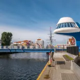 Niebieski most nad Regą w malowniczym mieście. W tle żaglowiec i nowoczesna architektura.