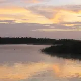 Zachód słońca nad rzeką, z mgłą unoszącą się nad wodą i zarysem lasu na horyzoncie.