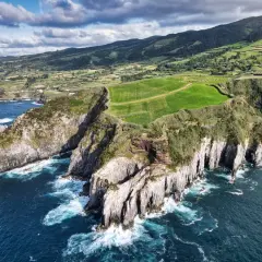 Zielone pola i strome klify na wyspach portugalskich, gdzie ocean rozbija się o skały.