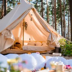 Wygodny namiot w lesie, z łóżkiem i dekoracjami. To właśnie glamping co to – luksusowy kemping w otoczeniu natury.