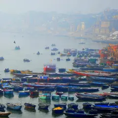 Tłum łodzi na rzece Ganges, z miastem w tle.