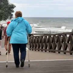 Kobieta z kijkami do nordic walking spaceruje promenadą nad morzem. Może to być część pobytu w dobrym sanatorium nad morzem NFZ.