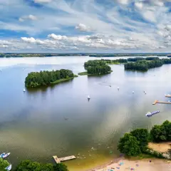 Malownicze jezioro z wyspami i żaglówkami, przypominające piękno wszystkich województw w Polsce.