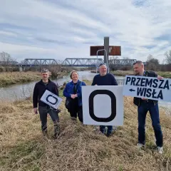 Cztery osoby stoją nad rzeką, trzymając tablice. Jedna z nich głosi "Przemysza Wisła", wskazując na źródło Wisły.