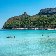 Turkusowa woda, plaża i zatoka pełna jachtów. W oddali widać wzgórza, a na jednym z nich wieżę. To widok na stolicę Sardynii, Cagliari.