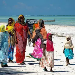 Kobiety w kolorowych strojach spacerują po plaży. Czy Zanzibar to państwo? Tak, to autonomiczny region Tanzanii.
