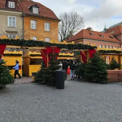 Jarmark świąteczny Warszawa: drewniane budki ozdobione choinkami i lampkami, ludzie spacerują wśród świątecznych dekoracji.