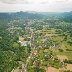 Widok z lotu ptaka na rozciągającą się w dolinie wieś, otoczoną zielonymi wzgórzami i lasami. To może być najdłuższa wieś w Polsce, z domami wzdłuż krętej drogi.