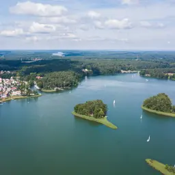Malowniczy widok na jedno z najpiękniejszych jezior w Polsce, z wyspami, żaglówkami i miasteczkiem na brzegu.