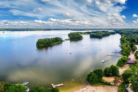 Malownicze jezioro z wyspami i żaglówkami, przypominające piękno wszystkich województw w Polsce.