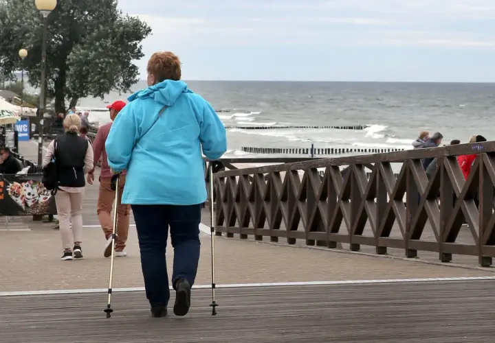 Kobieta z kijkami do nordic walking spaceruje promenadą nad morzem. Może to być część pobytu w dobrym sanatorium nad morzem NFZ.