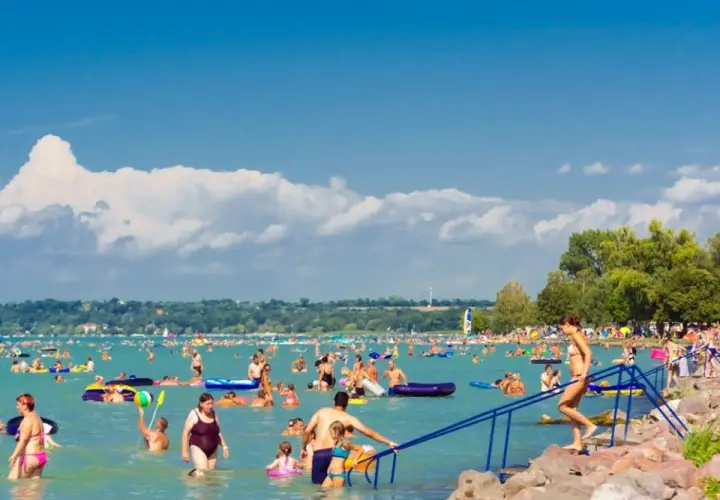 Tłum ludzi cieszy się słońcem i wodą na zatłoczonej Balaton plaży. Dzieci i dorośli pływają, relaksują się na materacach i bawią się w wodzie.