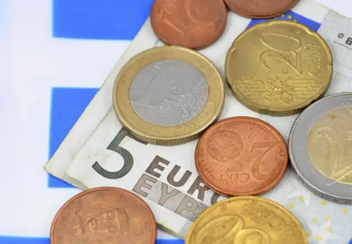 Euro to waluta w Grecji. Monety i banknot 5 euro na tle greckiej flagi.