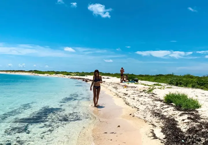 Kobieta spaceruje brzegiem turkusowej wody na plaży w Zatoce Meksykańskiej. W tle widać innych plażowiczów i bujną zieleń.