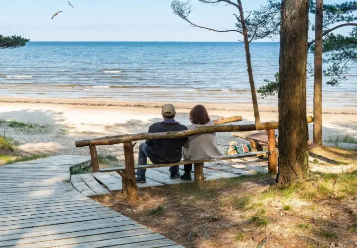 Para relaksująca para siedzi na ławce, patrząc na morze. Idealne miejsce na sanatoria nad morzem.