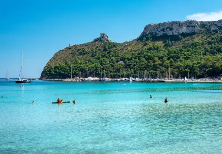 Turkusowa woda, plaża i zatoka pełna jachtów. W oddali widać wzgórza, a na jednym z nich wieżę. To widok na stolicę Sardynii, Cagliari.