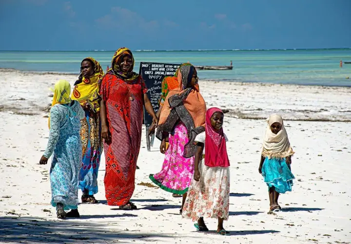 Kobiety w kolorowych strojach spacerują po plaży. Czy Zanzibar to państwo? Tak, to autonomiczny region Tanzanii.
