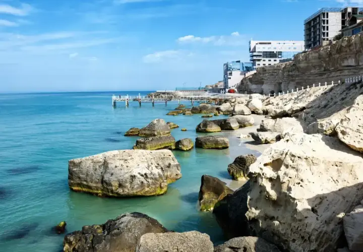 Brzeg Kaspijskiego Morza, największego jeziora na świecie, z kamienistą plażą, klifami i nowoczesnymi budynkami.