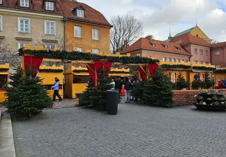 Jarmark świąteczny Warszawa: drewniane budki ozdobione choinkami i lampkami, ludzie spacerują wśród świątecznych dekoracji.