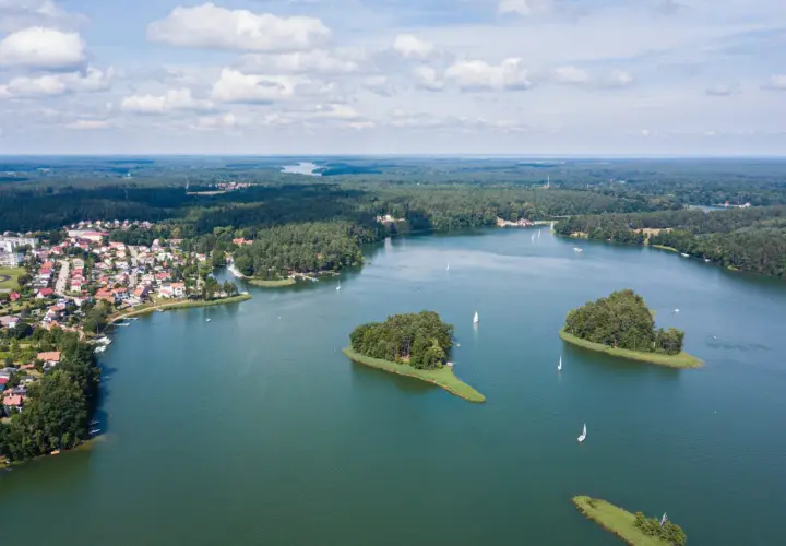 Malowniczy widok na jedno z najpiękniejszych jezior w Polsce, z wyspami, żaglówkami i miasteczkiem na brzegu.