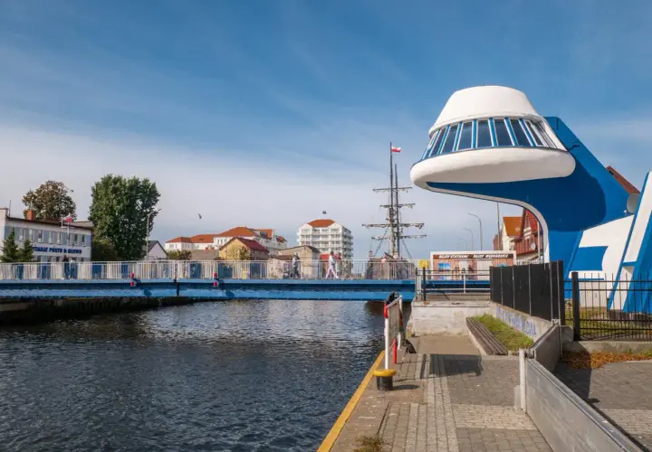 Niebieski most nad Regą w malowniczym mieście. W tle żaglowiec i nowoczesna architektura.