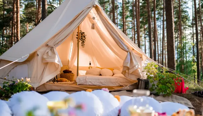 Wygodny namiot w lesie, z łóżkiem i dekoracjami. To właśnie glamping co to – luksusowy kemping w otoczeniu natury.