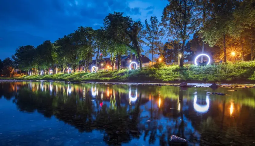 Nocny spacer wzdłuż rzeki, gdzie świetliste kręgi odbijają się w wodzie. Magiczna atmosfera, która płynie przez Cieszyn.