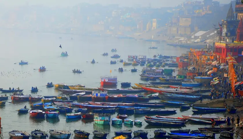 Tłum łodzi na rzece Ganges, z miastem w tle.