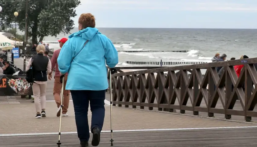Kobieta z kijkami do nordic walking spaceruje promenadą nad morzem. Może to być część pobytu w dobrym sanatorium nad morzem NFZ.