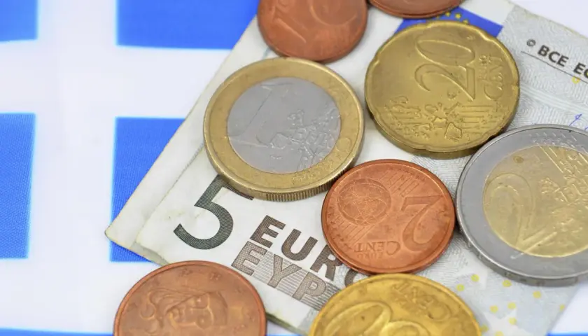 Euro to waluta w Grecji. Monety i banknot 5 euro na tle greckiej flagi.