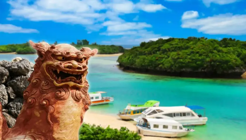 Kamienna lwica strzeże rajskiej plaży z łodziami na turkusowej wodzie. Archipelag z Okinawą w tle, z bujną zielenią i błękitnym niebem.