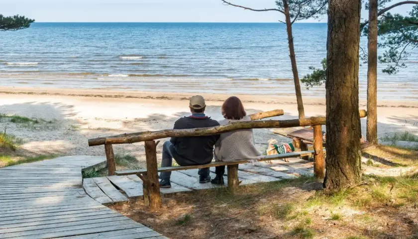 Para relaksująca para siedzi na ławce, patrząc na morze. Idealne miejsce na sanatoria nad morzem.