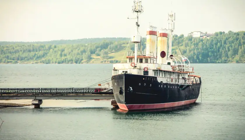 Stary statek "Angara" cumuje przy nabrzeżu. W tle zielone wzgórza i spokojna woda. Port nad Angarą.