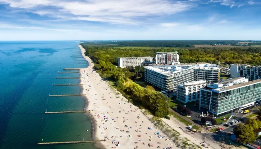 Nowoczesny hotel 5 gwiazdkowy nad morzem z widokiem na plażę pełną wypoczywających.