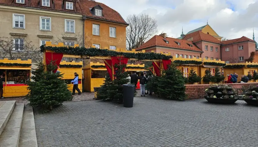 Jarmark świąteczny Warszawa: drewniane budki ozdobione choinkami i lampkami, ludzie spacerują wśród świątecznych dekoracji.