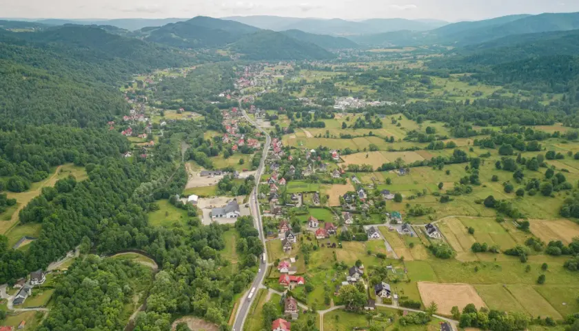 Widok z lotu ptaka na rozciągającą się w dolinie wieś, otoczoną zielonymi wzgórzami i lasami. To może być najdłuższa wieś w Polsce, z domami wzdłuż krętej drogi.