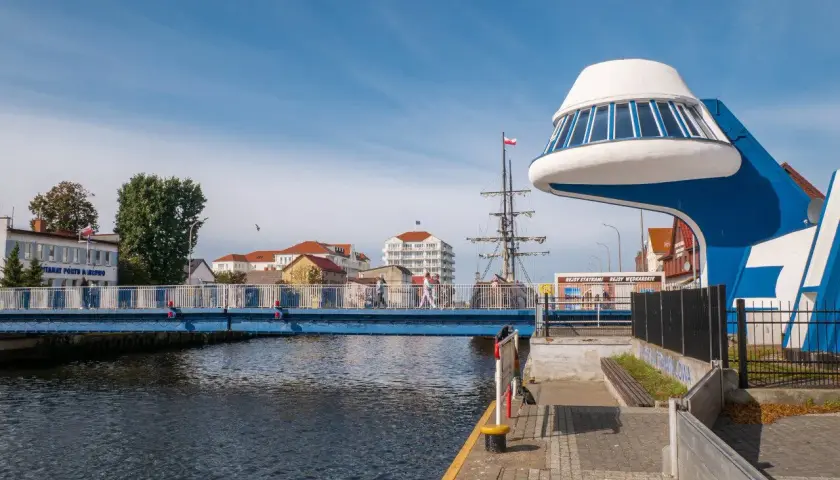 Niebieski most nad Regą w malowniczym mieście. W tle żaglowiec i nowoczesna architektura.
