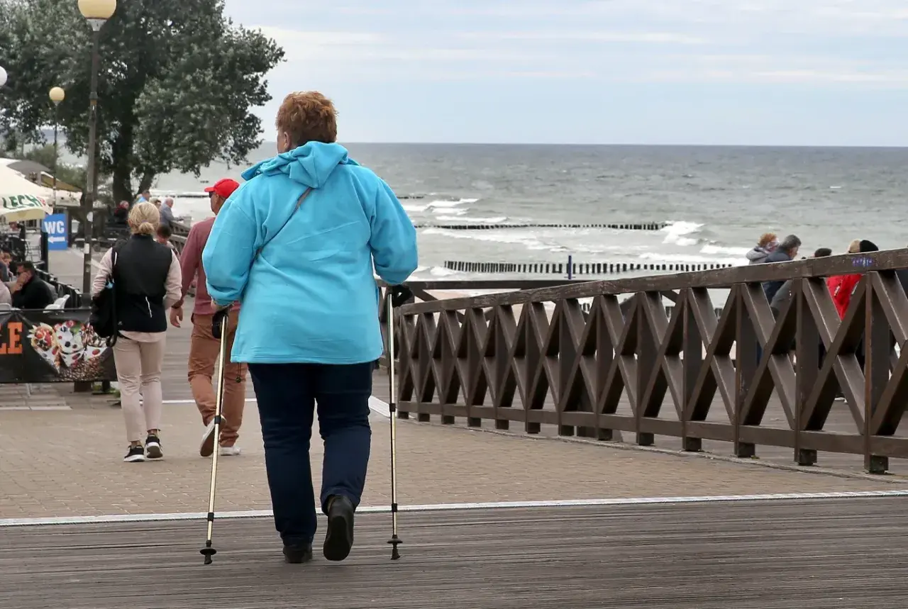 Kobieta z kijkami do nordic walking spaceruje promenadą nad morzem. Może to być część pobytu w dobrym sanatorium nad morzem NFZ.