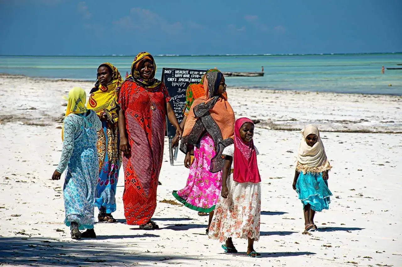 Kobiety w kolorowych strojach spacerują po plaży. Czy Zanzibar to państwo? Tak, to autonomiczny region Tanzanii.
