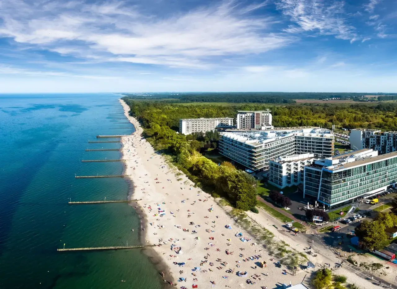 Nowoczesny hotel 5 gwiazdkowy nad morzem z widokiem na plażę pełną wypoczywających.
