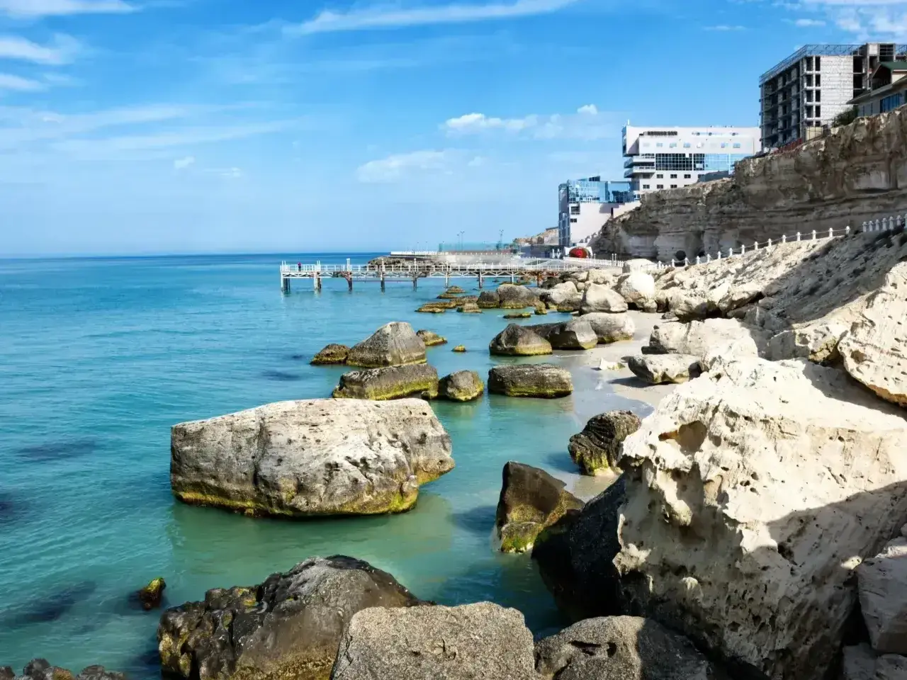 Brzeg Kaspijskiego Morza, największego jeziora na świecie, z kamienistą plażą, klifami i nowoczesnymi budynkami.