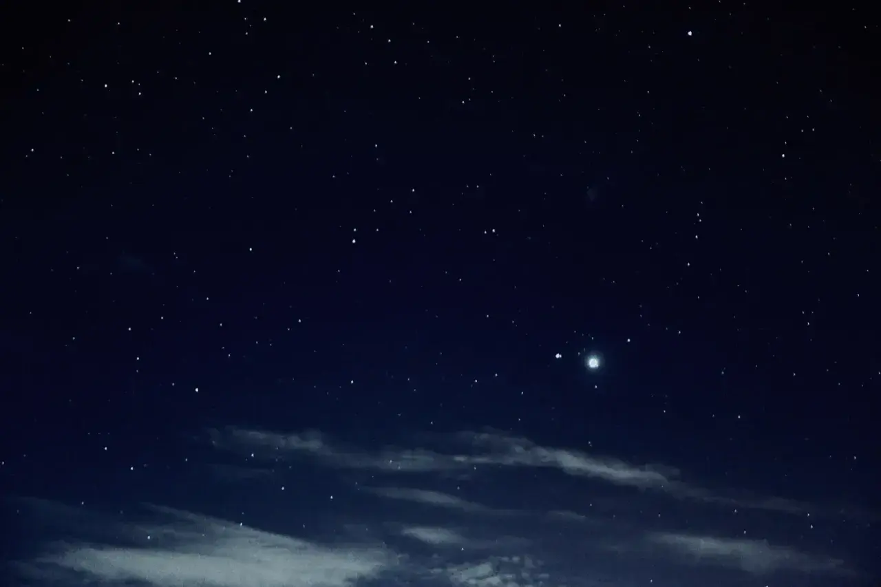 Gwieździste niebo nocą, z widocznym jasnym obiektem, być może planetą, podczas nowiu księżyca.