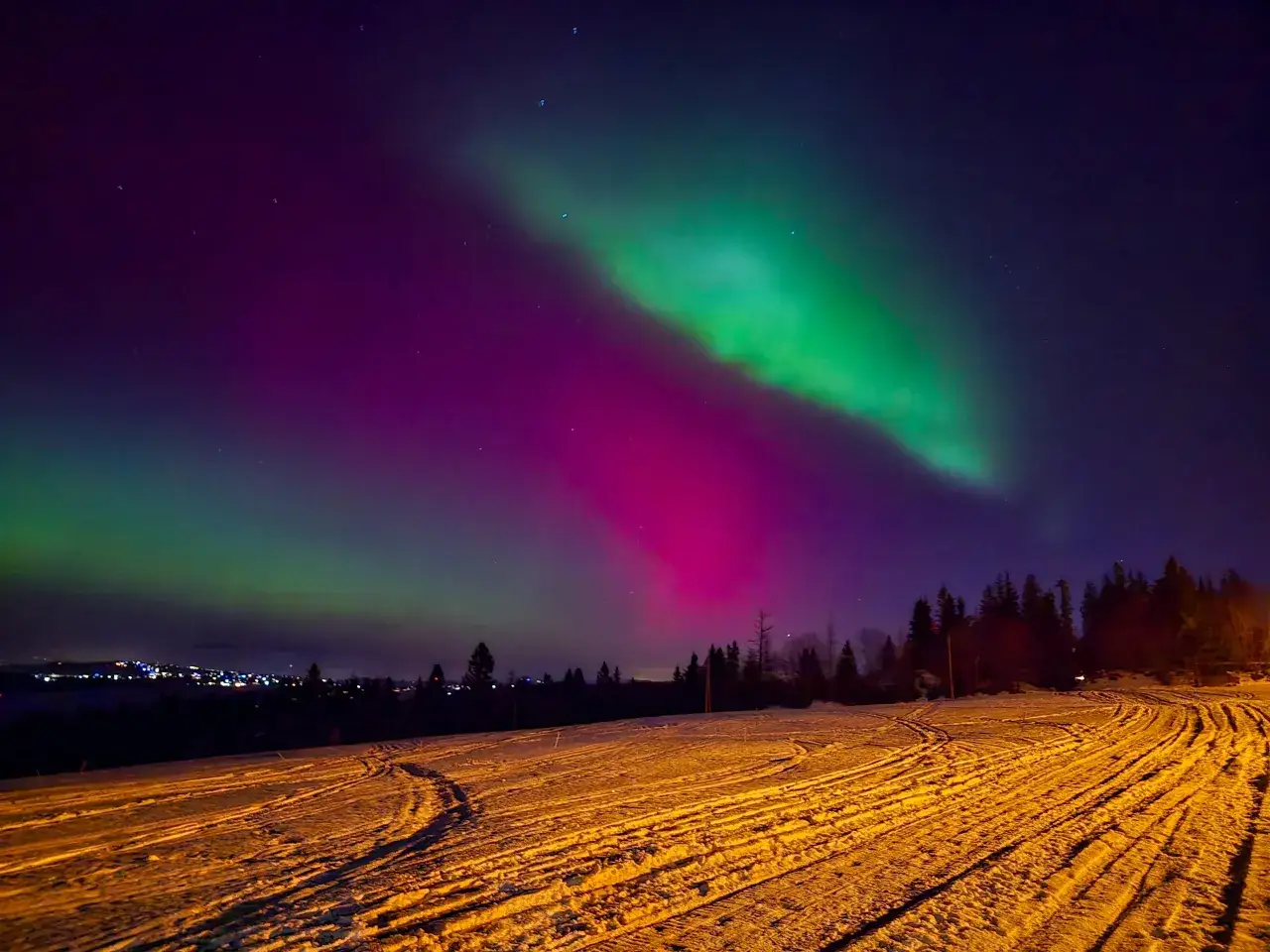 Nocne niebo nad ośnieżonym krajobrazem rozświetla zorza polarna, ukazując piękno tego, jak powstaje zorza polarna.