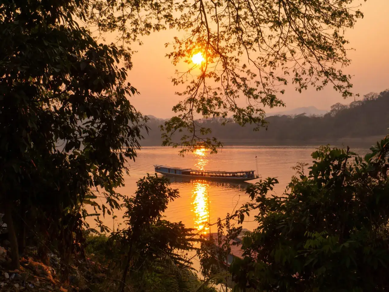 Zachód słońca nad Mekongiem, w tle góry i łódź. To widok z Luang Prabang, stolicy Laosu.