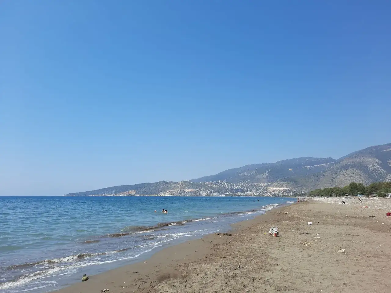 Słoneczny dzień nad morzem w Finike. Błękitne niebo, spokojne fale i piaszczysta plaża z widokiem na góry.